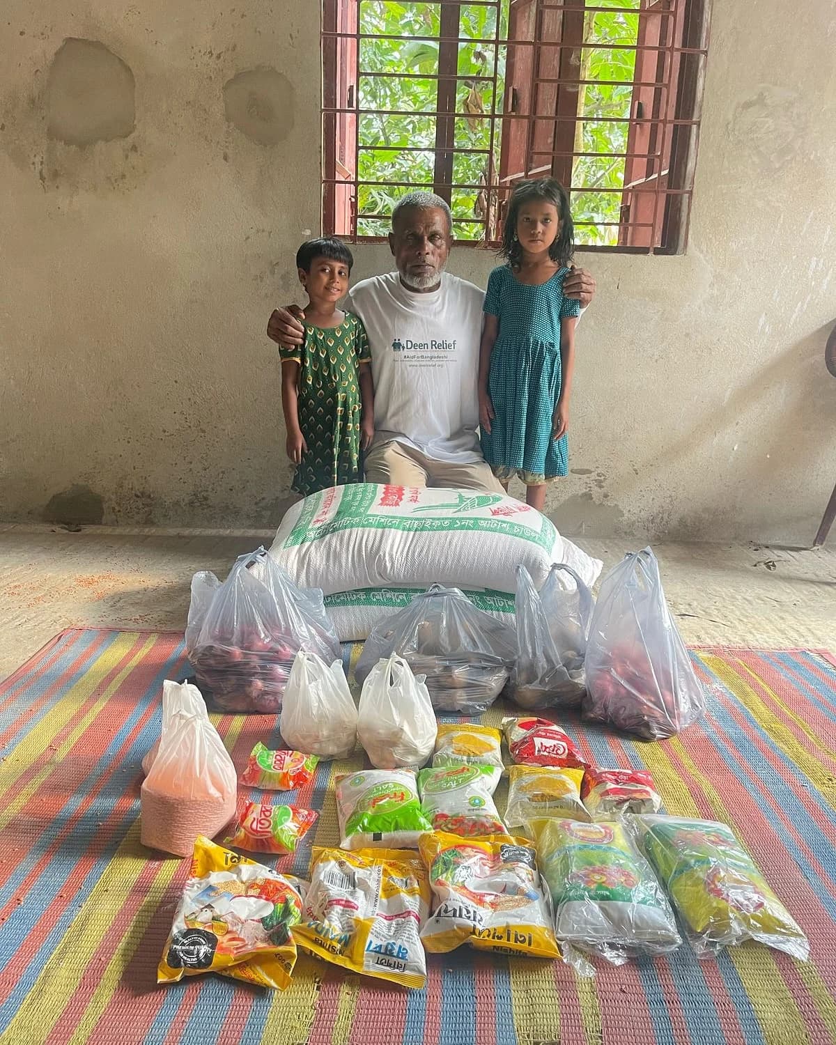 A Deen Relief field worker with two girls and food supplies during aid distribution in rural Bangladesh
