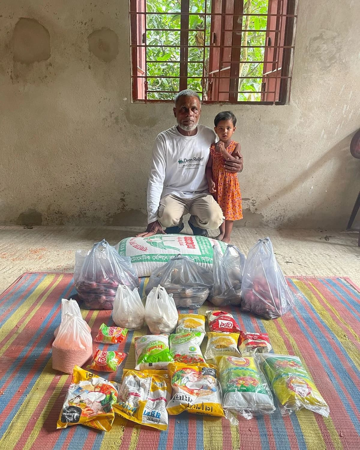 A Deen Relief field worker with a young girl and food supplies during aid distribution in rural Bangladesh
