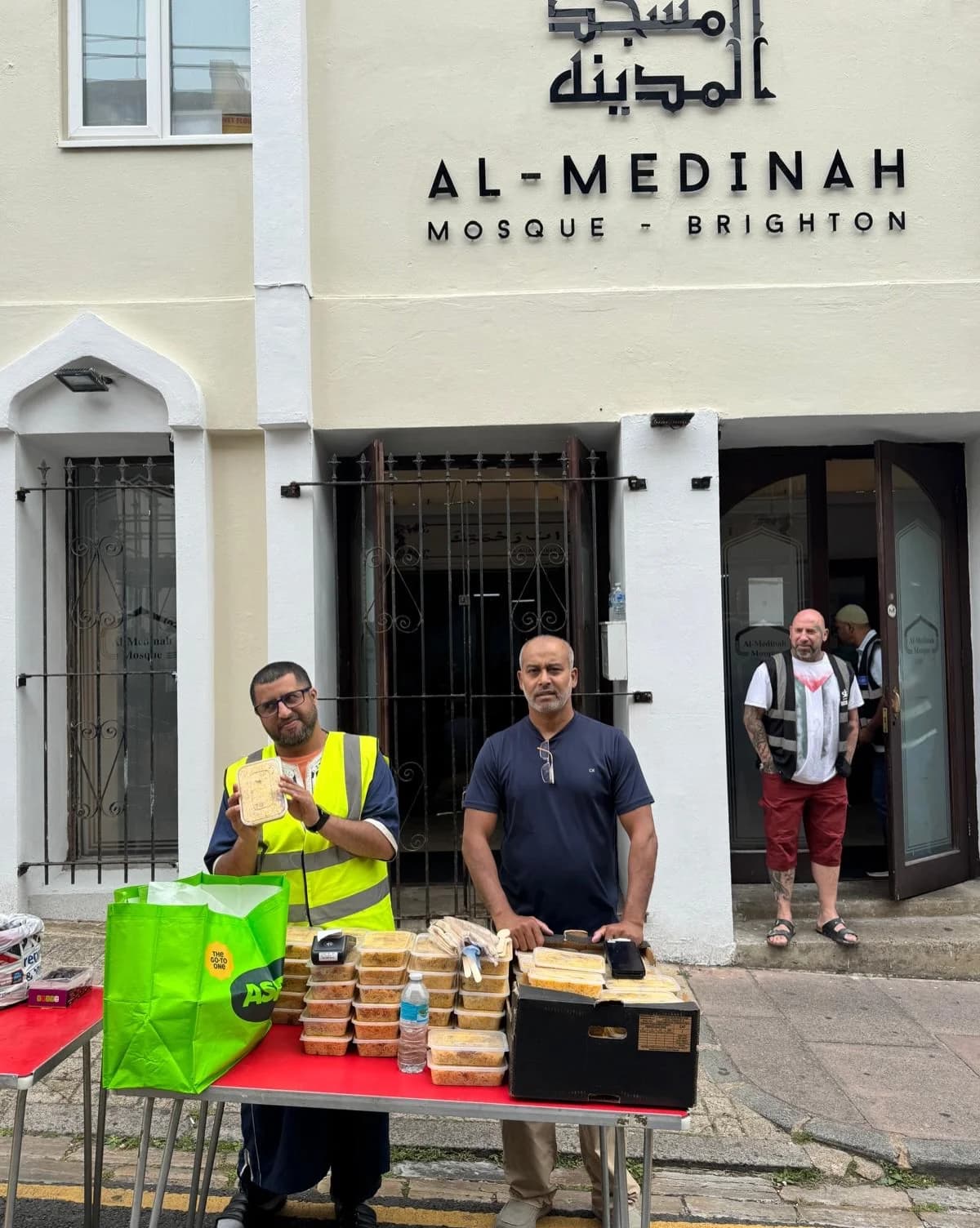 Deen Relief volunteers in hi-vis vests distributing food outside Al-Medinah Mosque, Brighton